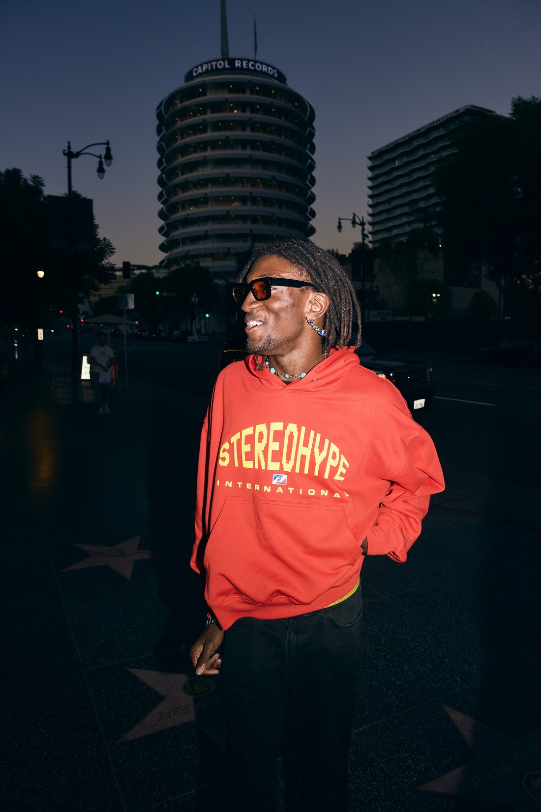 Solo portrait in red STEREOHYPE INTERNATIONAL hoodie at golden hour, Capitol Records building